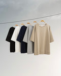Five shirts in black, white, navy, gray, and beige hanging on a line against a light gray background.