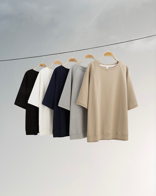 Five shirts in black, white, navy, gray, and beige hanging on a line against a light gray background.